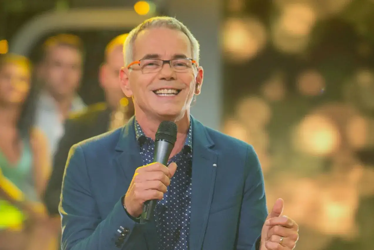 Uśmiechnięty prowadzący z mikrofonem, w tle rozmyte postacie. Czy to powód, dlaczego fani bojkotują nową odsłonę programu Jaka to melodia?