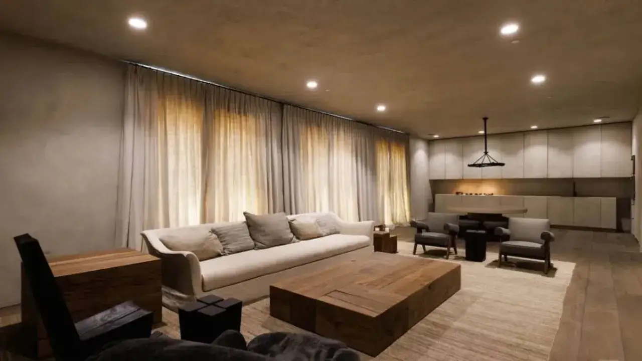 Soggiorno minimalista con divano bianco, tavolino in legno grezzo e tende color crema. L'arredamento del **kim kardashian house** &egrave; essenziale e moderno.