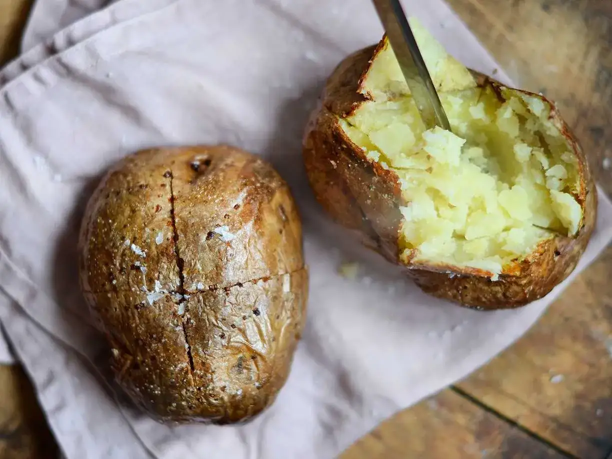 Perfekt bakad potatis i airfryer, en &auml;r uppskuren och visar det fluffiga inkr&aring;met. Saltkorn glittrar p&aring; den gyllene ytan.