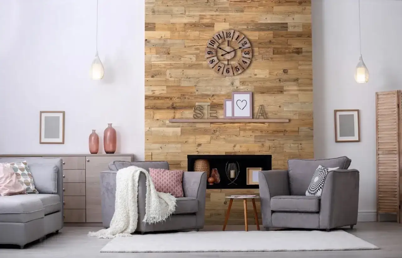 Salon chaleureux avec mur en bois brut, cheminée, fauteuils gris et horloge. L'essence de bois réchauffe l'atmosphère.