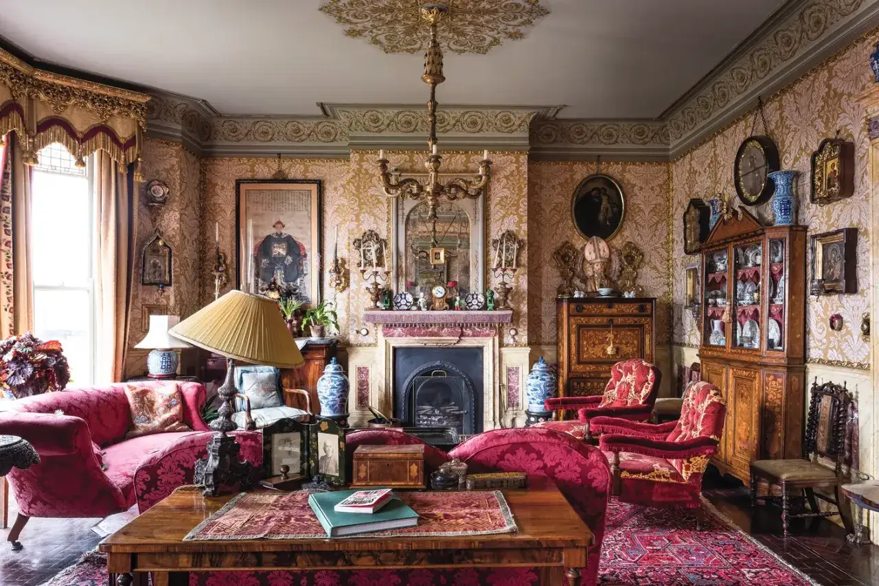 Bogato zdobiony salon w stylu wiktoriańskim. Czerwone meble, złote ornamenty i wzorzyste tapety tworzą atmosferę epoki.