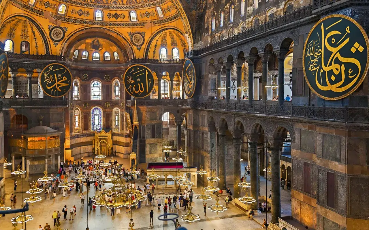 Imponerande interiör av Hagia Sofia i Istanbul med stora runda kalligrafiska inskriptioner och många besökare som beundrar den storslagna arkitekturen.