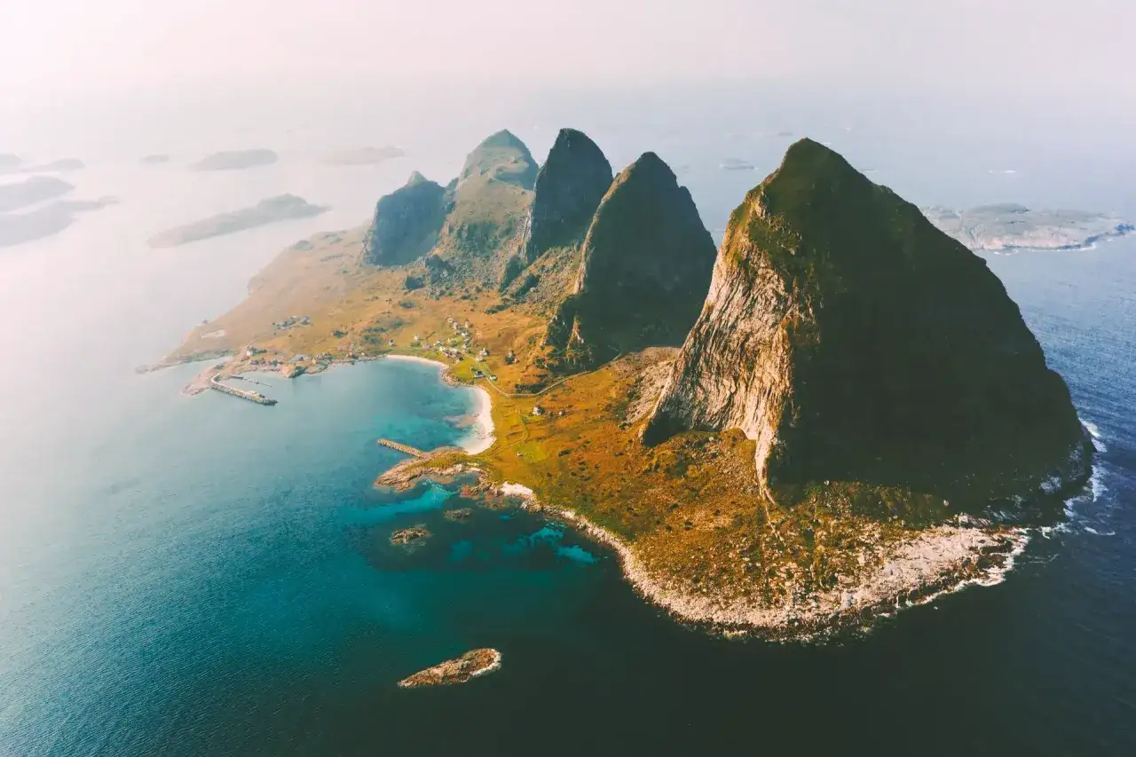 En dramatisk kustlinje med spetsiga berg och en liten by vid havet. En idyllisk plats att **träna Norge** på, med frisk luft och hisnande vyer.