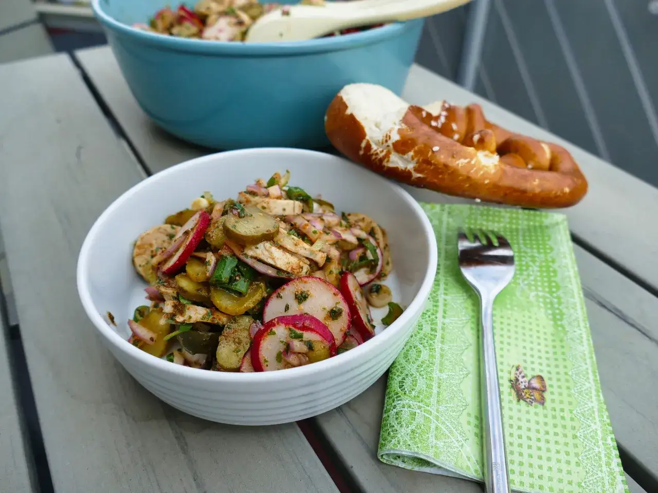 Frischer Salat mit Radieschen, Gurken und Zwiebeln, perfekt als Beilage zum Bratwurst-Genuss. Dazu ein Brezel und eine Gabel.
