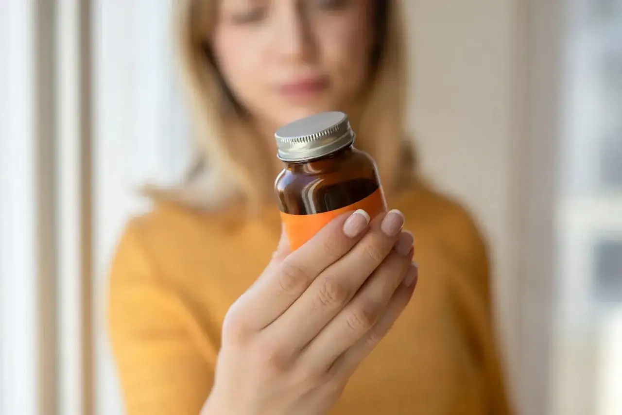 Frau prüft die Dosierung auf einem Fläschchen. Sie fragt sich, wieviel Q10 am Tag optimal ist.
