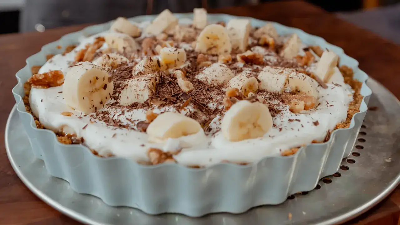 Délicieuse tarte banane caramel, garnie de rondelles de banane, de noix et de copeaux de chocolat.