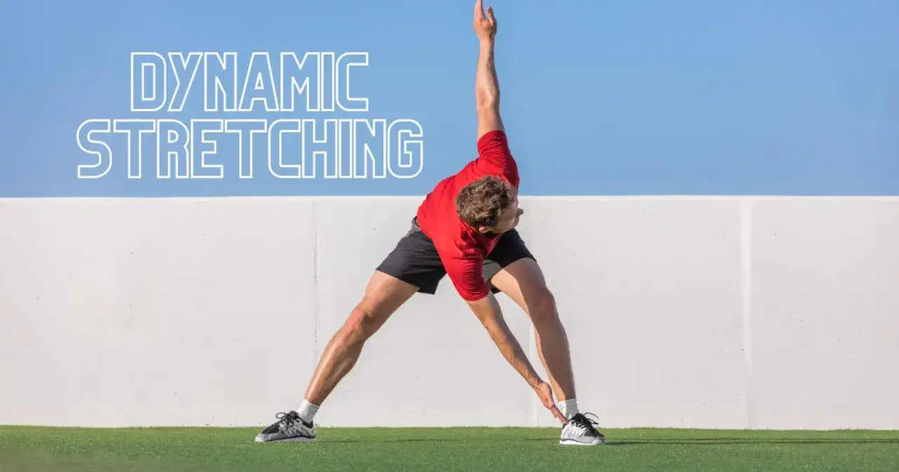 Man utför dynamisk stretching utomhus, med en vit vägg och blå himmel som bakgrund.