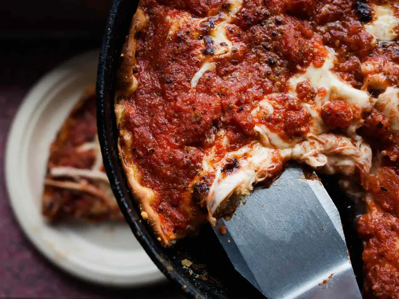 Ein Stück einer tiefen, saftigen Chicago Style Pizza wird mit einem Spachtel herausgehoben. Der Käse zieht Fäden.