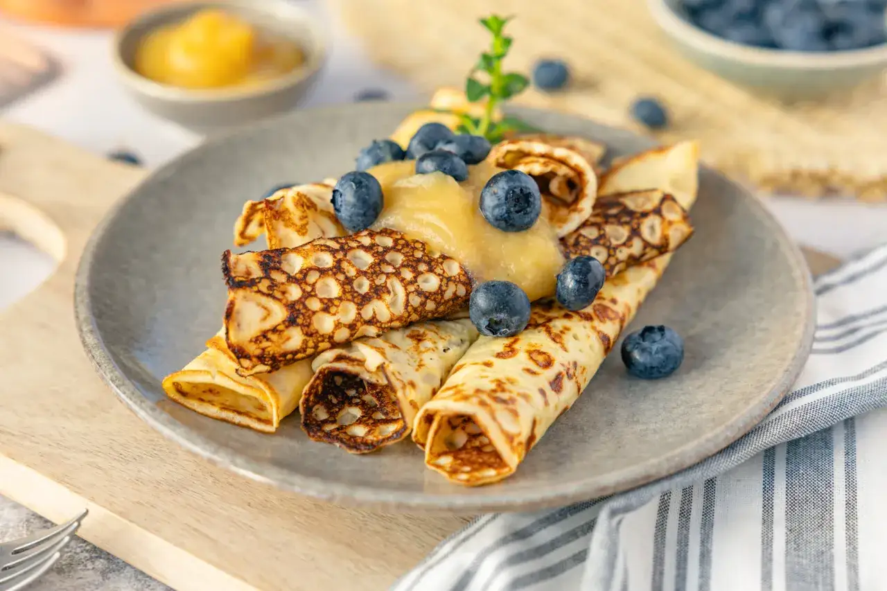 Quark Pfannkuchen mit Apfelmus und Blaubeeren auf einem grauen Teller, garniert mit frischer Minze.
