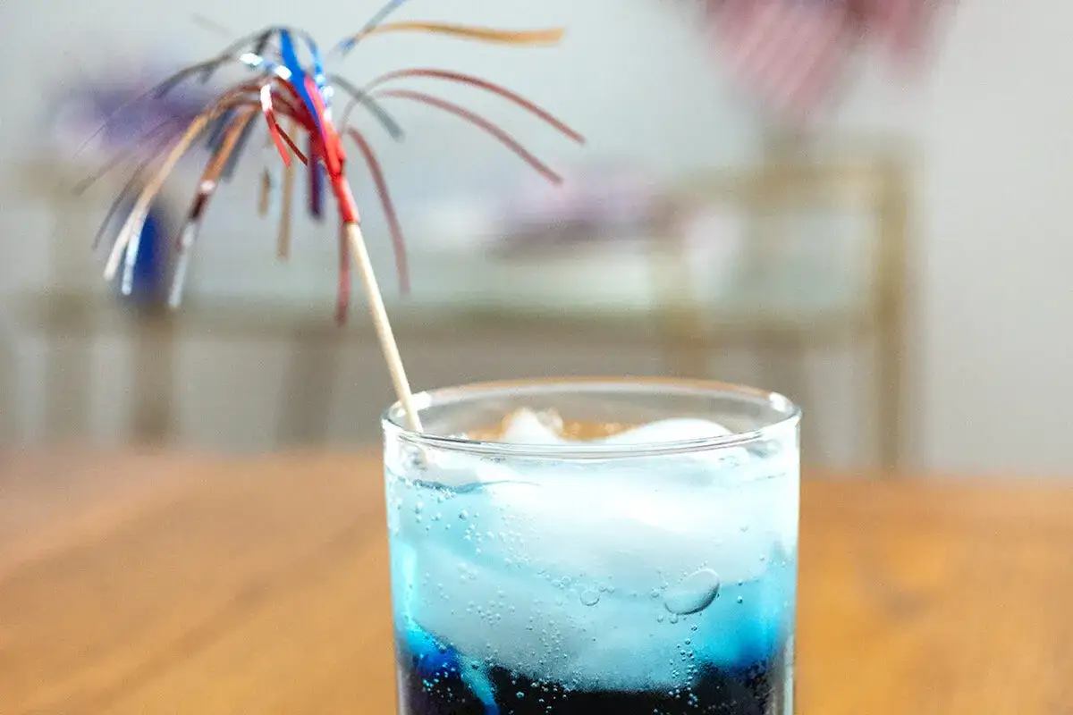 Orzeźwiający drink z grenadyną i blue curacao, ozdobiony patyczkiem z kolorowymi wstążkami.