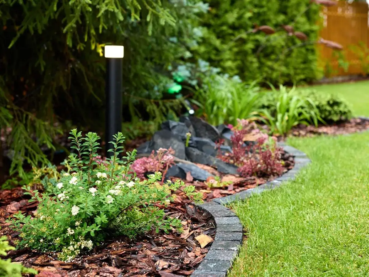 Moderne Beeteinfassung Ideen mit Stein und Mulch, beleuchtet durch eine Gartenleuchte.
