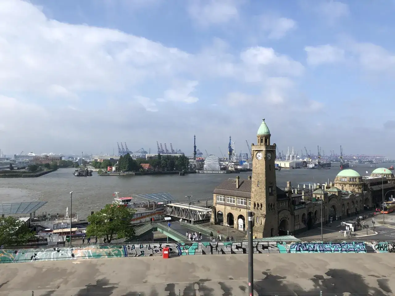 Hamburger Hafen mit Landungsbrücken und dem markanten Stintfang-Turm. Kräne und Schiffe im Hintergrund.