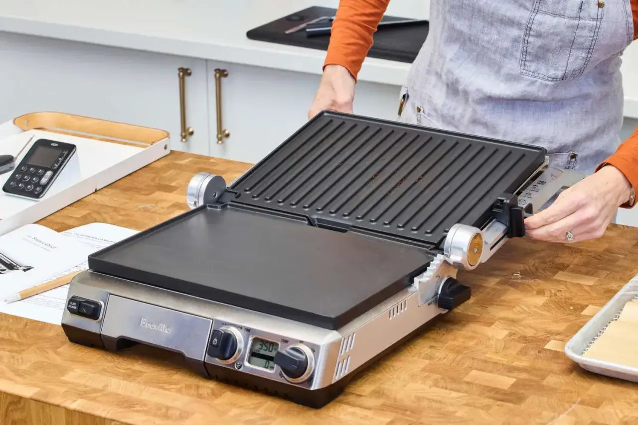 Otwarty grill elektryczny Breville, gotowy do użycia. Instrukcja obsługi i termometr leżą obok. Dowiedz się, jak grillować na grillu elektrycznym.