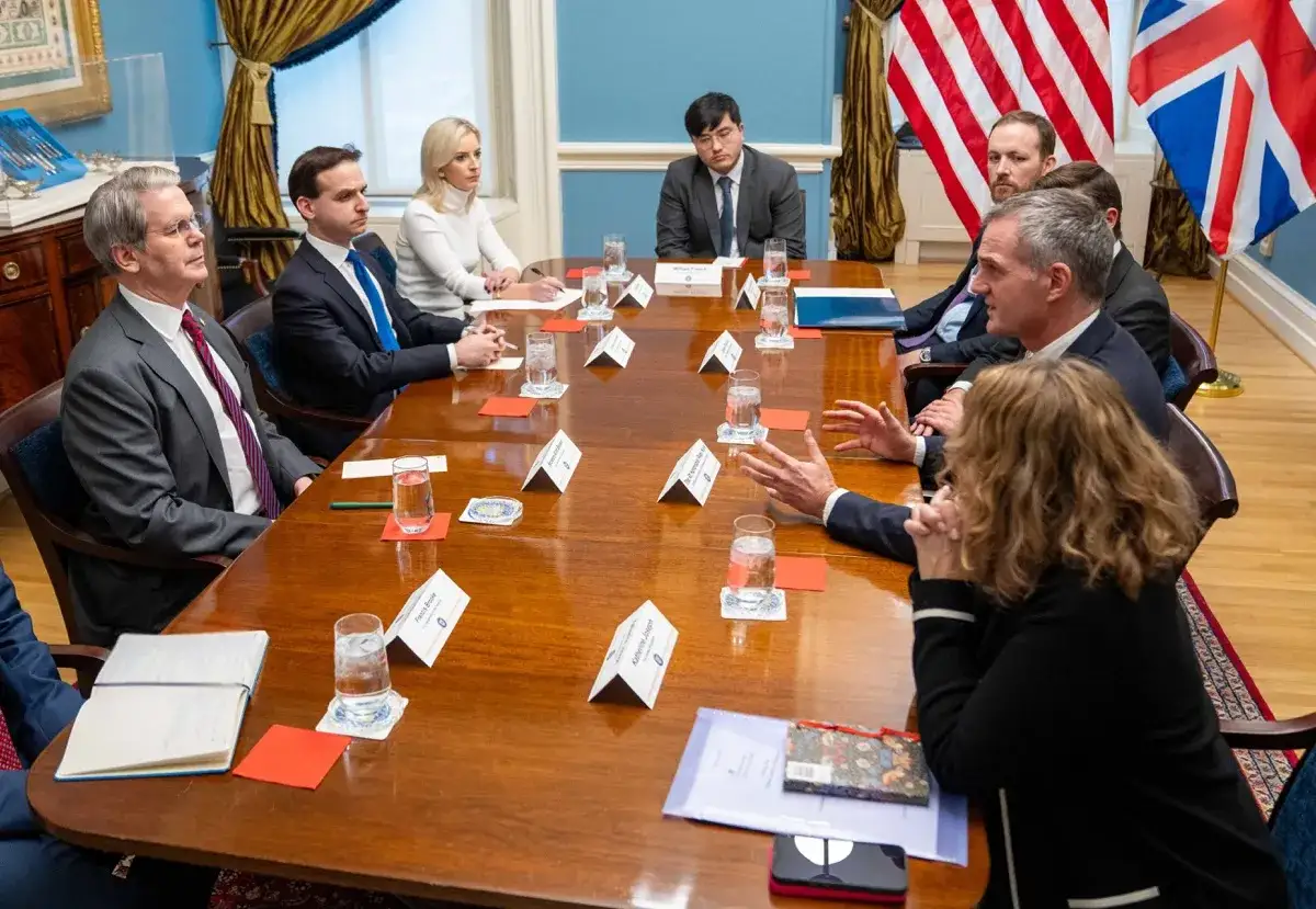 A group of people sit around a polished wooden table, engaged in discussion. The scene evokes a sense of reflection on change in the workplace as they collaborate.