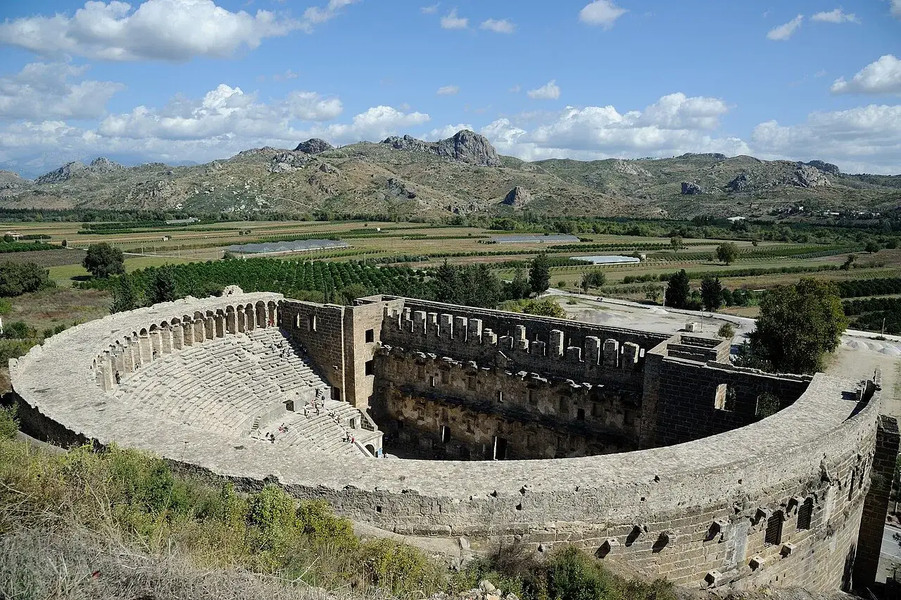 Starożytny teatr Aspendos, z widokiem na zielone pola i góry, zachwyca swoją architekturą.