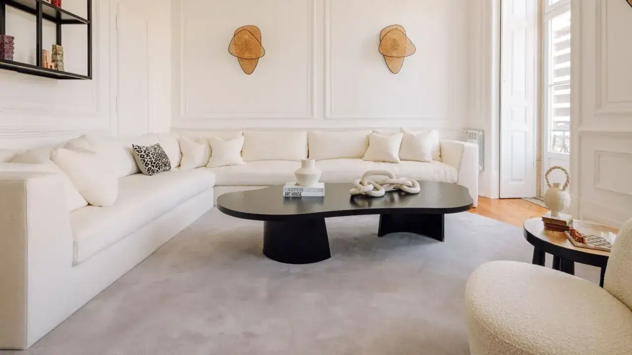 Sof&aacute; blanco roto y alfombra gris claro. Mesa de centro negra con decoraci&oacute;n, mostrando la diferencia entre blanco y blanco roto.