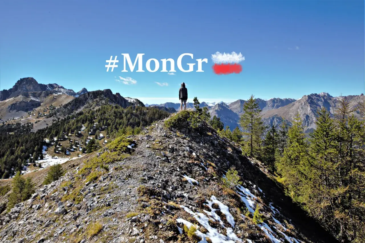Vue panoramique sur les montagnes du Queyras, avec un randonneur au sommet et le hashtag #MonGr.