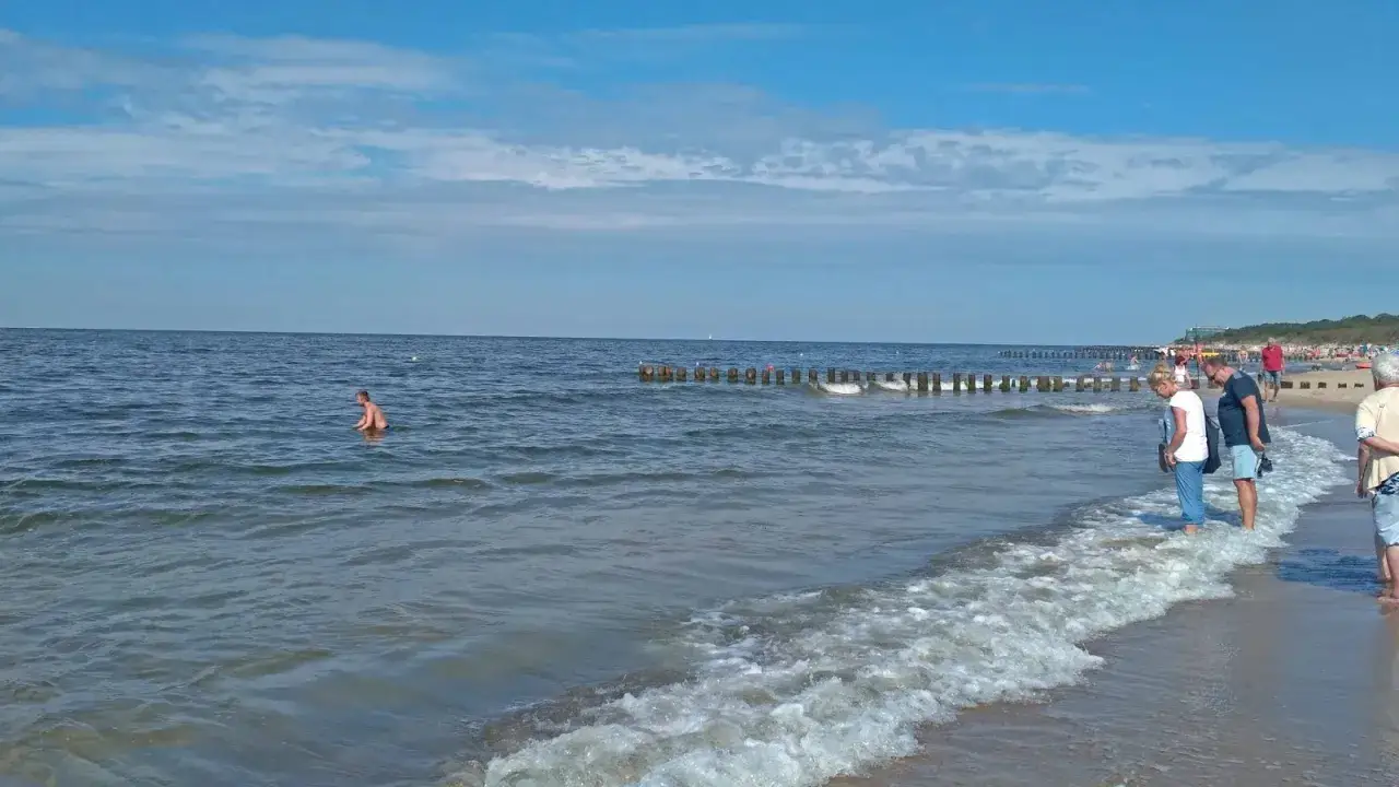 Spokojna plaża w Dziwnowie, z falującym morzem i ludźmi cieszącymi się słońcem. To jedne z wielu atrakcji Dziwnowa.