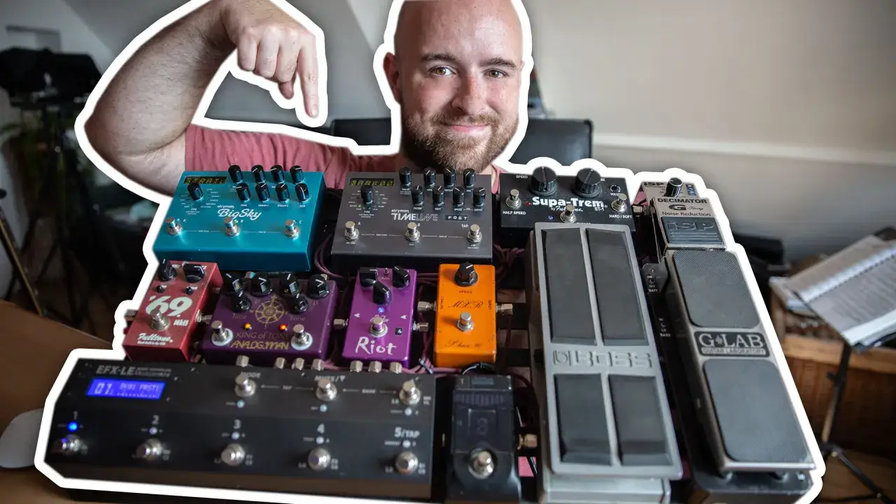 Uśmiechnięty mężczyzna prezentuje swoją rozbudowaną pedalboardę, pokazując kolejność efektów gitarowych.