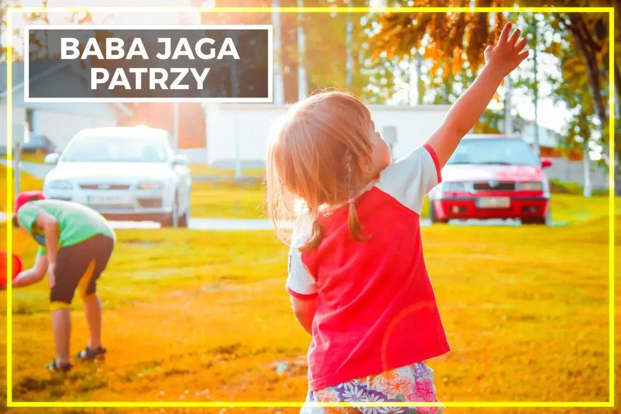 Dzieci bawią się na trawie, a dziewczynka z podniesioną ręką woła: 
