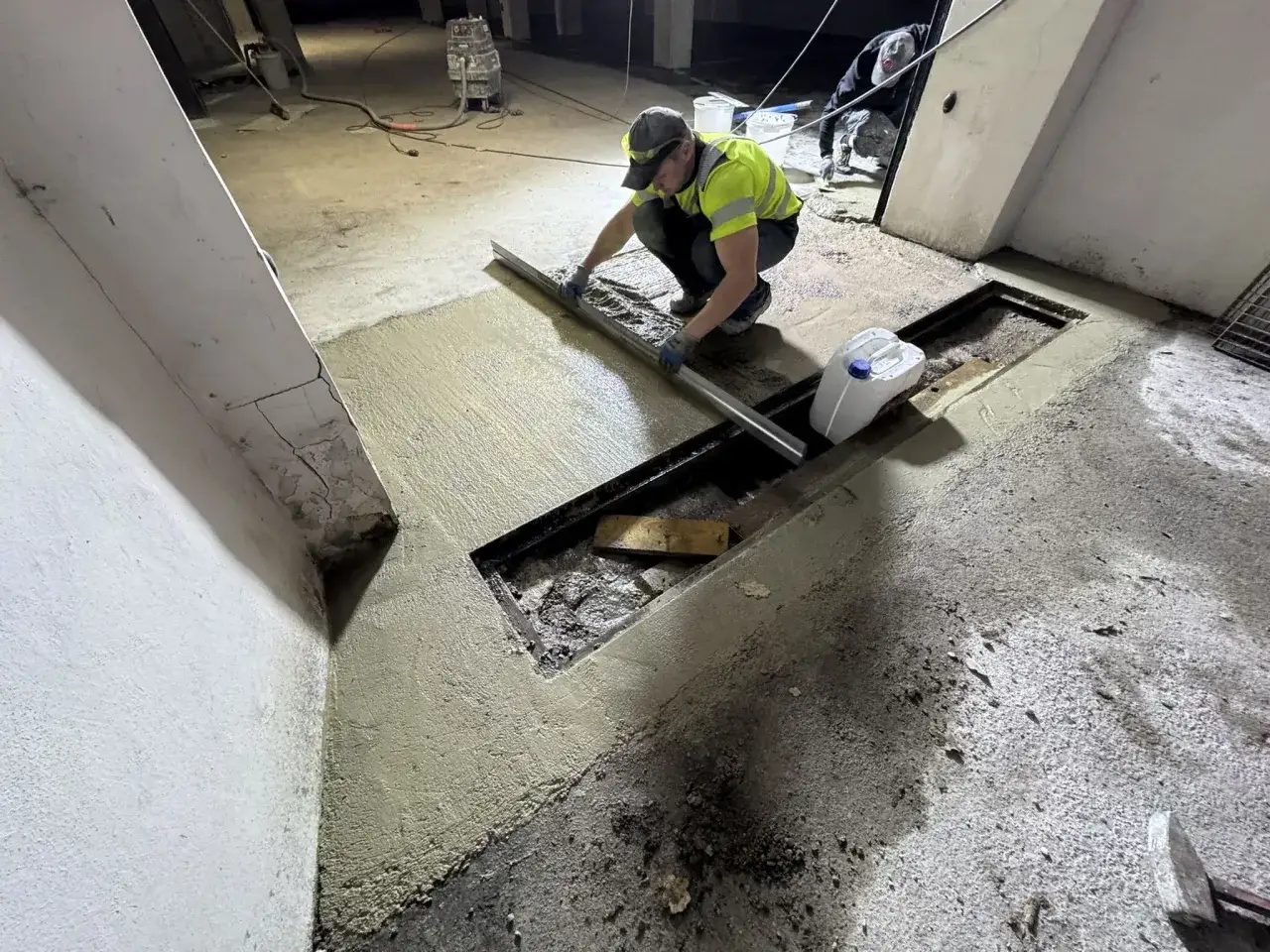 Pracownik wykonuje naprawę posadzki betonowej, wyrównując świeżą masę za pomocą łaty.
