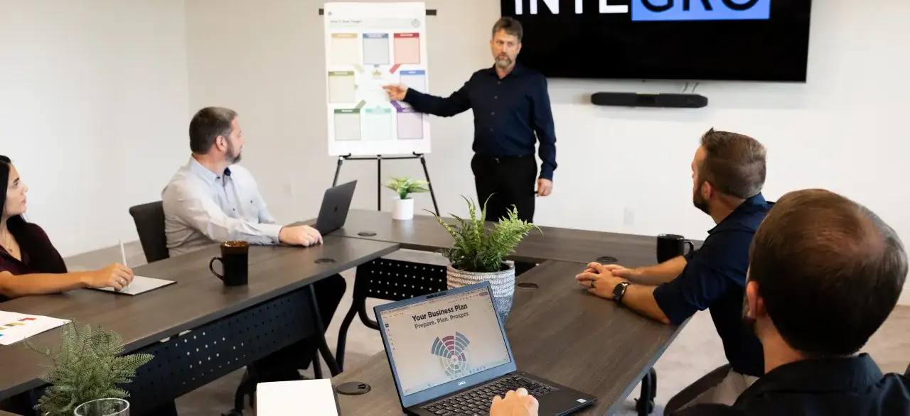 A leader points to a business plan chart, demonstrating the qualities of a good leader: clear vision and effective communication during a team meeting.