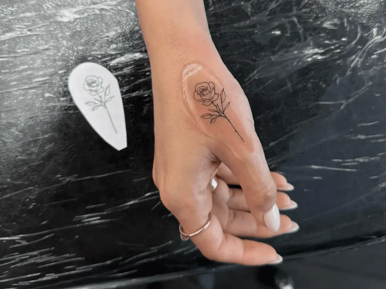 Una mano con un tatuaje de rosa en proceso. El diseño, similar a una plantilla de amoxicilina, se está aplicando.