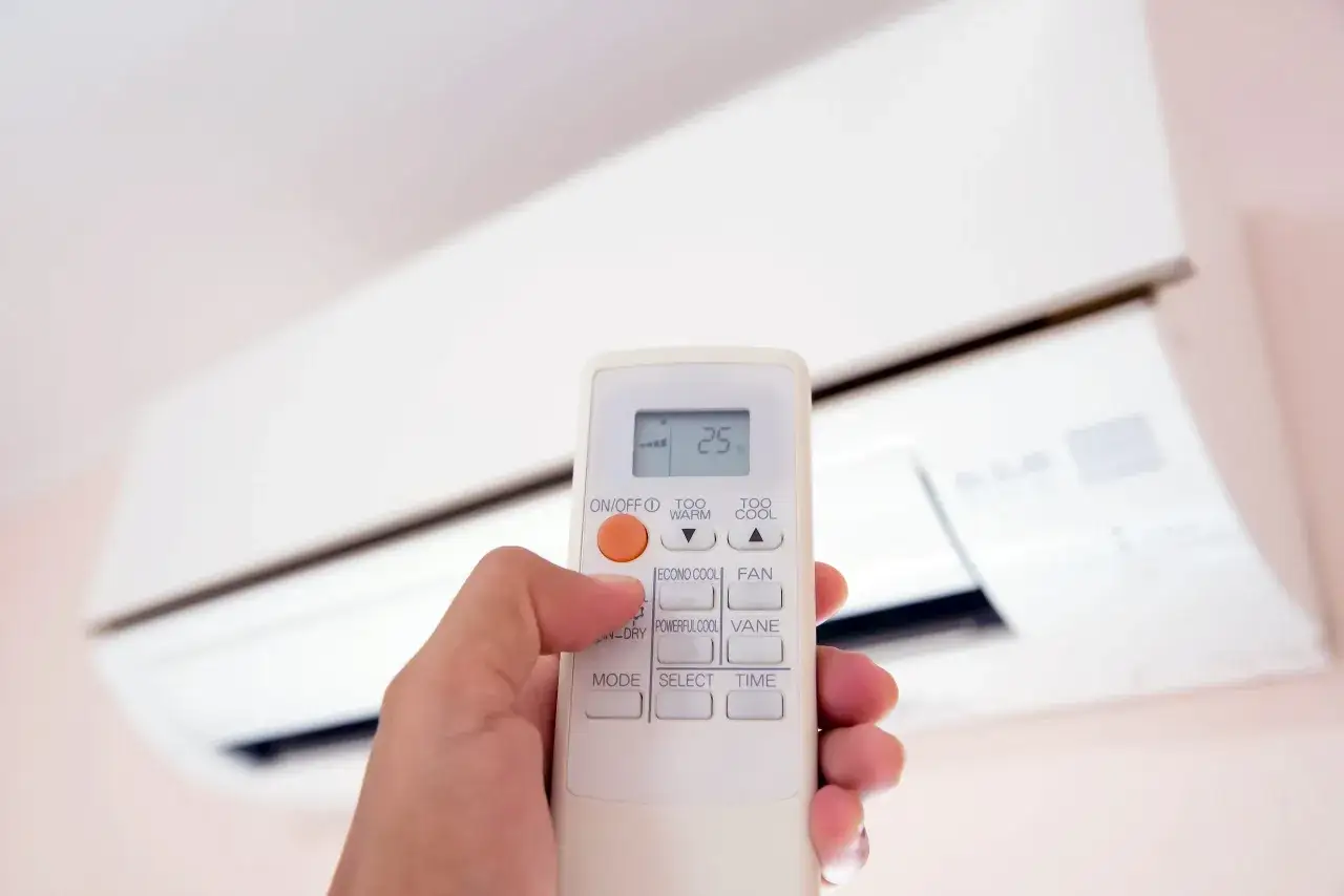 Mano ajustando el control remoto del aire acondicionado a 25&deg;C. La pregunta es a cuanto poner el aire acondicionado en verano para estar c&oacute;modo.