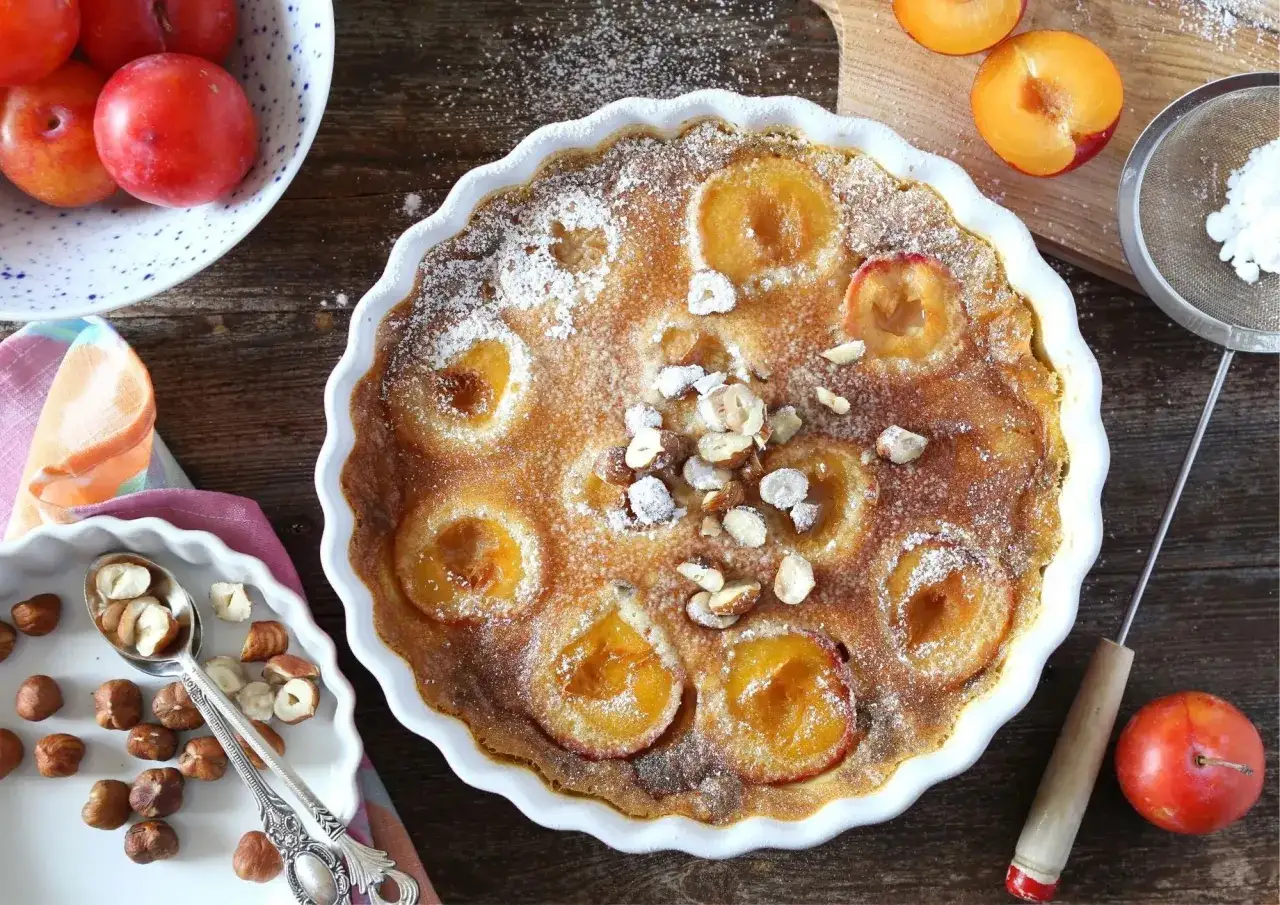 Un d&eacute;licieux clafoutis aux prunes, saupoudr&eacute; de sucre glace et garni de noisettes concass&eacute;es, pr&ecirc;t &agrave; &ecirc;tre d&eacute;gust&eacute;.