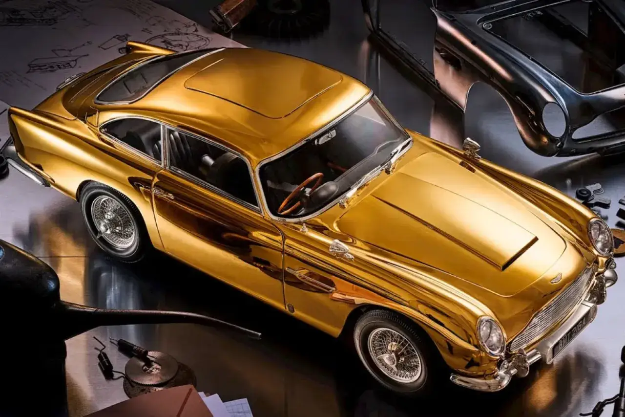 Złoty Aston Martin DB5 lśni jak skarb, otoczony narzędziami i szkicami, gotowy do akcji.