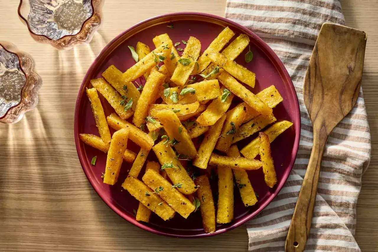Goldgelbe polenta sticks, knusprig gebraten und mit Kräutern bestreut, liegen auf einem Teller.