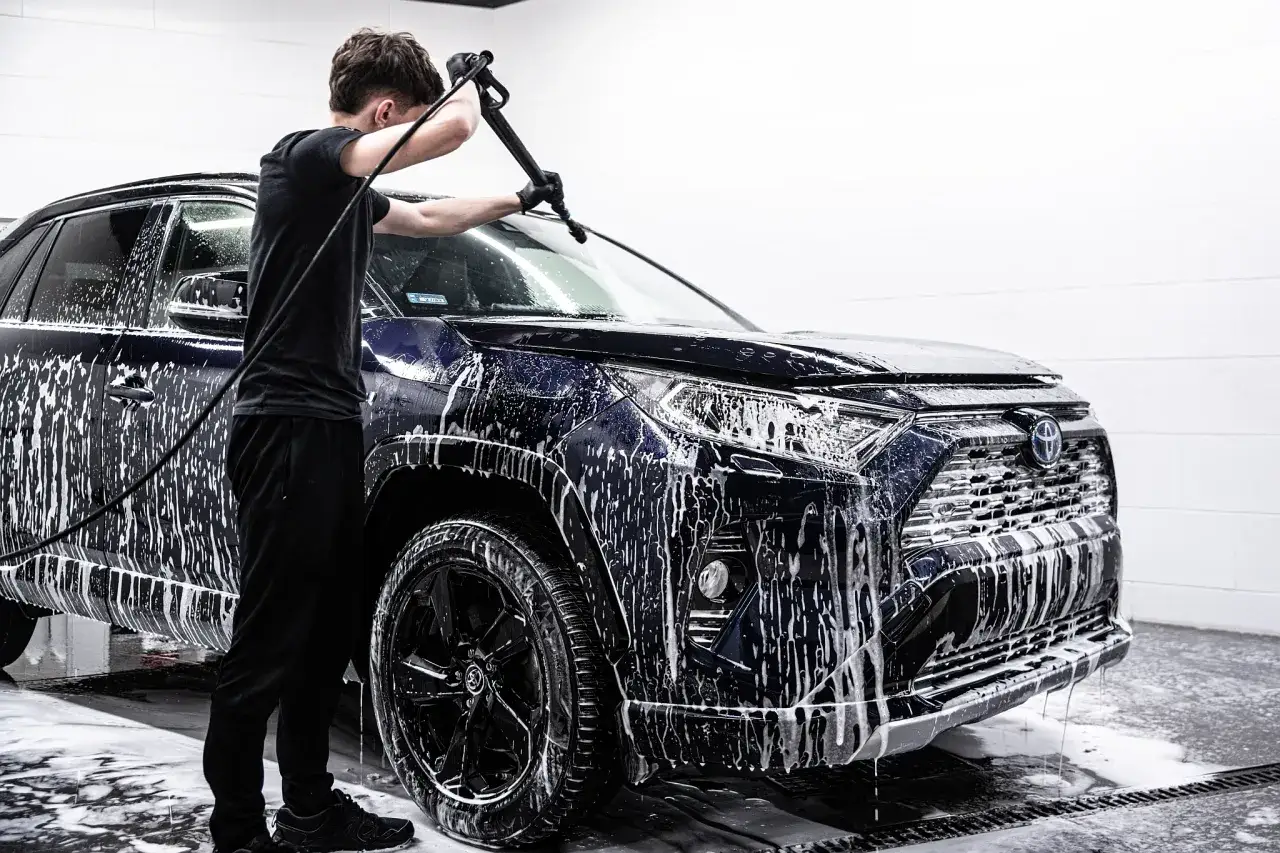Mężczyzna myje ciemny SUV pianą. Czy warto inwestować w auto detailing w warsztacie zamiast w tradycyjne mycie i wosk?