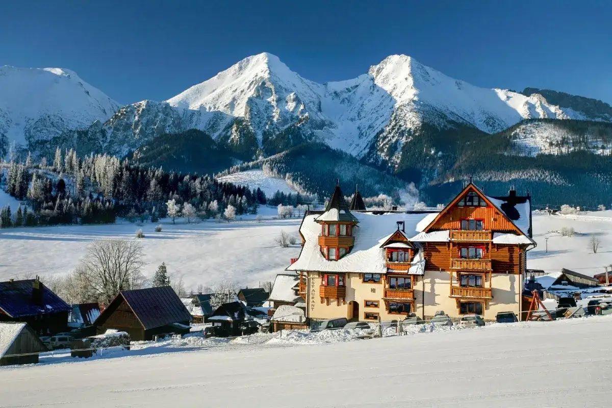 Zimowy krajobraz z budynkami i ośnieżonymi górami w tle. To idealne miejsce na wypoczynek w ski centrum Strachan.