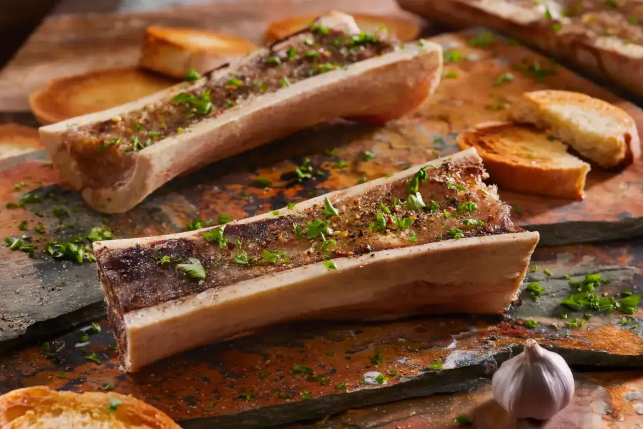 Os à moelle barbecue, grillés et parsemés de persil frais, accompagnés de toasts croustillants et d'une tête d'ail.