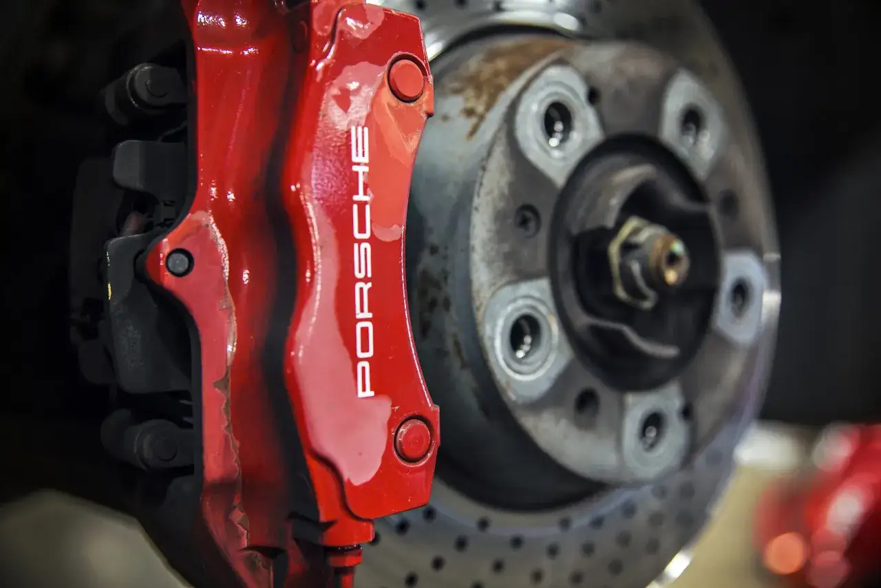 Roter Porsche-Bremssattel &uuml;ber gelochten Bremsscheiben. Gelochte Bremsscheiben Vorteil: bessere K&uuml;hlung und Bremsleistung.