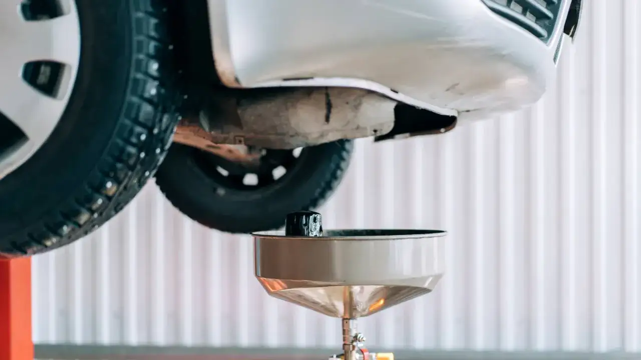 Vidange bo&icirc;te de vitesse manuelle : un filtre &agrave; huile usag&eacute; est pr&ecirc;t &agrave; &ecirc;tre retir&eacute; sous une voiture soulev&eacute;e.