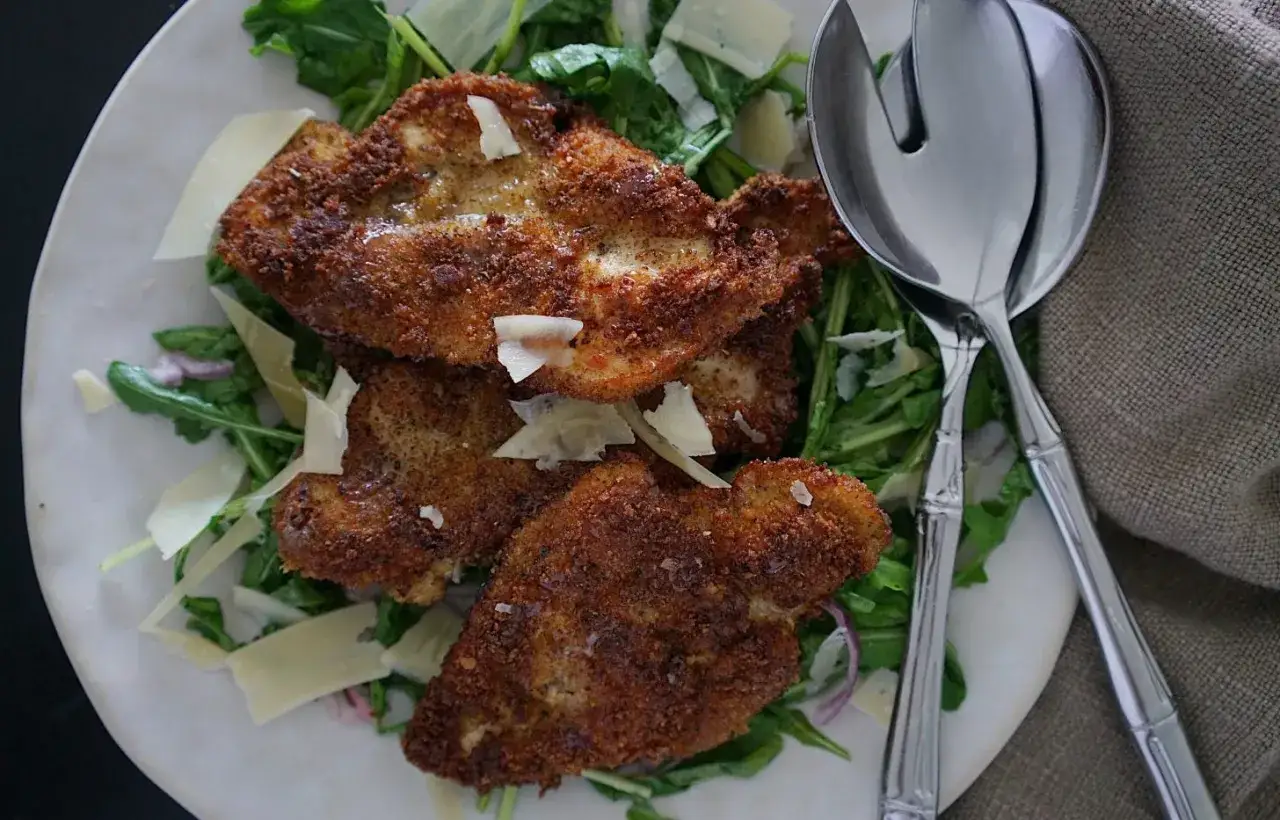 Straccetti di pollo dorati su un letto di rucola e scaglie di parmigiano.