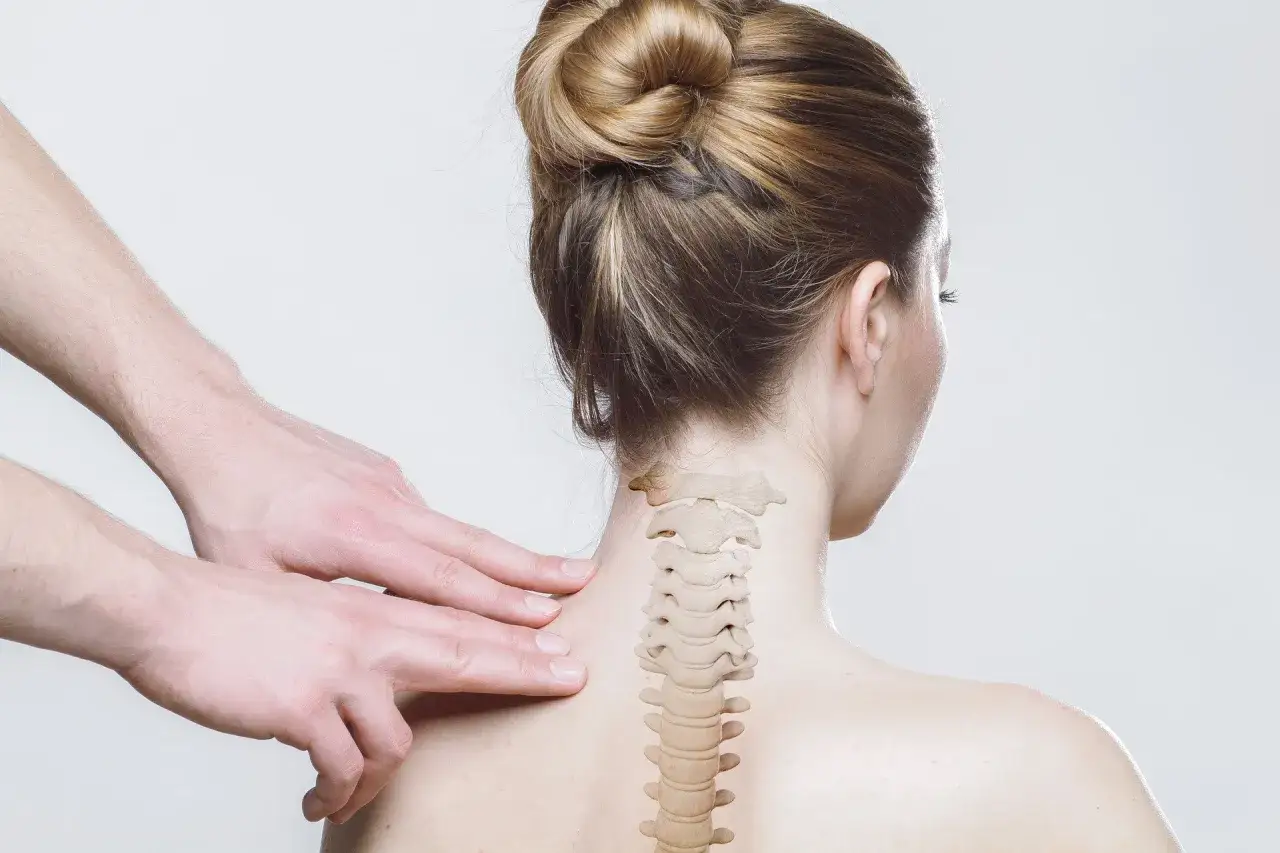 Dłonie terapeuty badają kręgosłup szyjny kobiety. Czy to objawy whiplash?