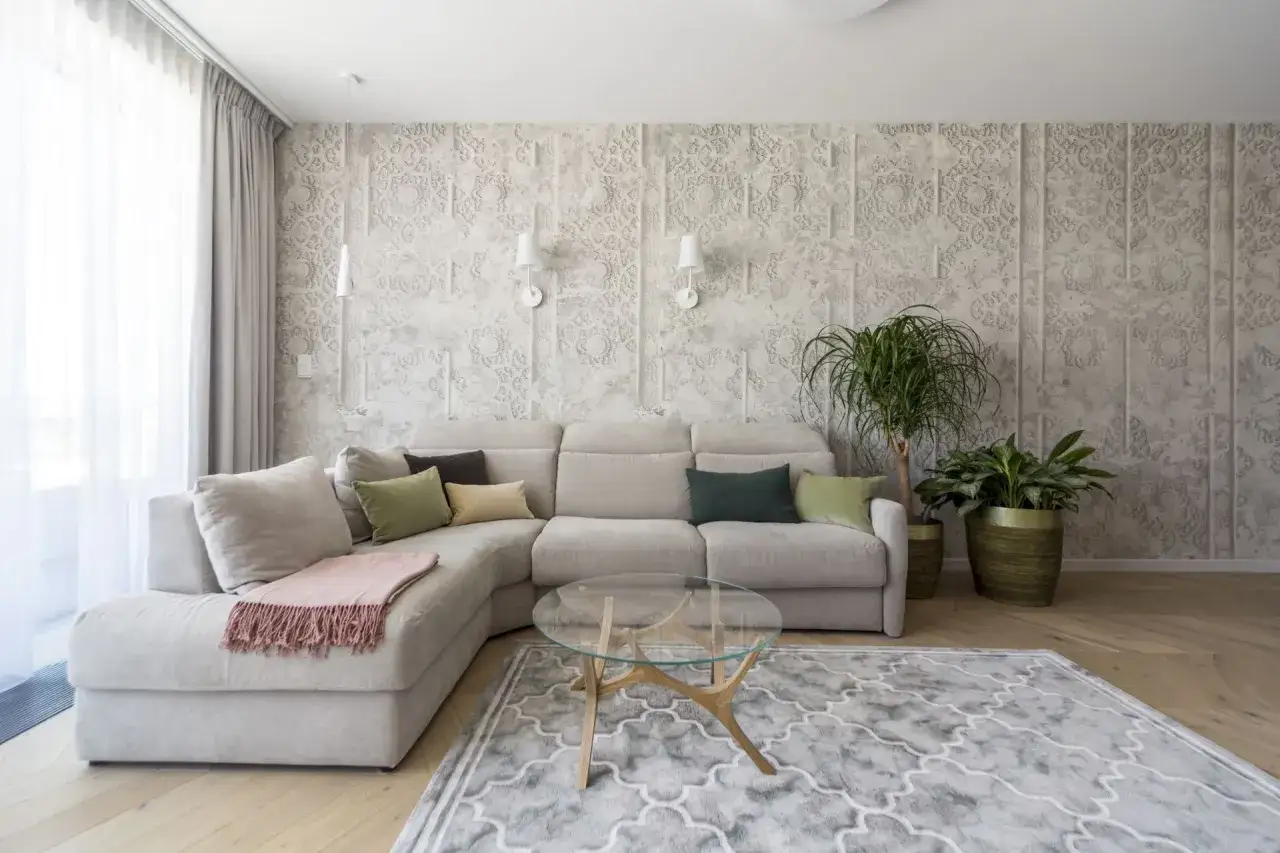 Elegancki salon z beżowo szarą tapetą o orientalnym wzorze, wygodną kanapą i szklanym stolikiem.