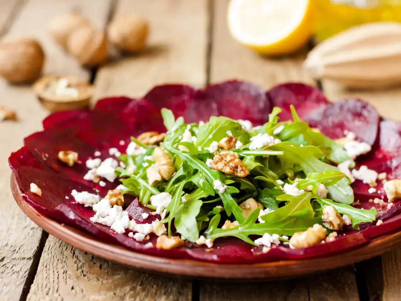 Rote Bete Carpaccio italienisch mit Rucola, Waln&uuml;ssen und Ziegenk&auml;se auf einem rustikalen Holztisch.