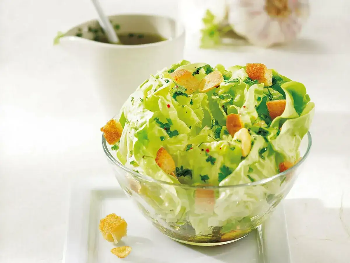 Frischer Kopfsalat mit Croutons und Kräutern, perfekt für ein leichtes Kopfsalat Rezept. Dazu eine kleine Kanne mit Dressing.