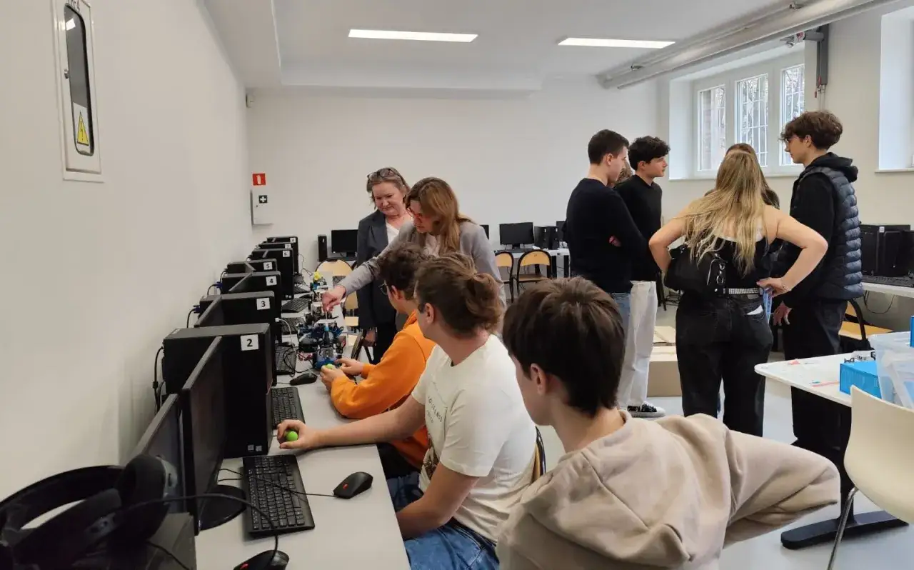Uczniowie i nauczyciele pracują przy robotach. Czy technik programista jest trudny? Zajęcia z robotyki pokazują, że nauka może być fascynująca.