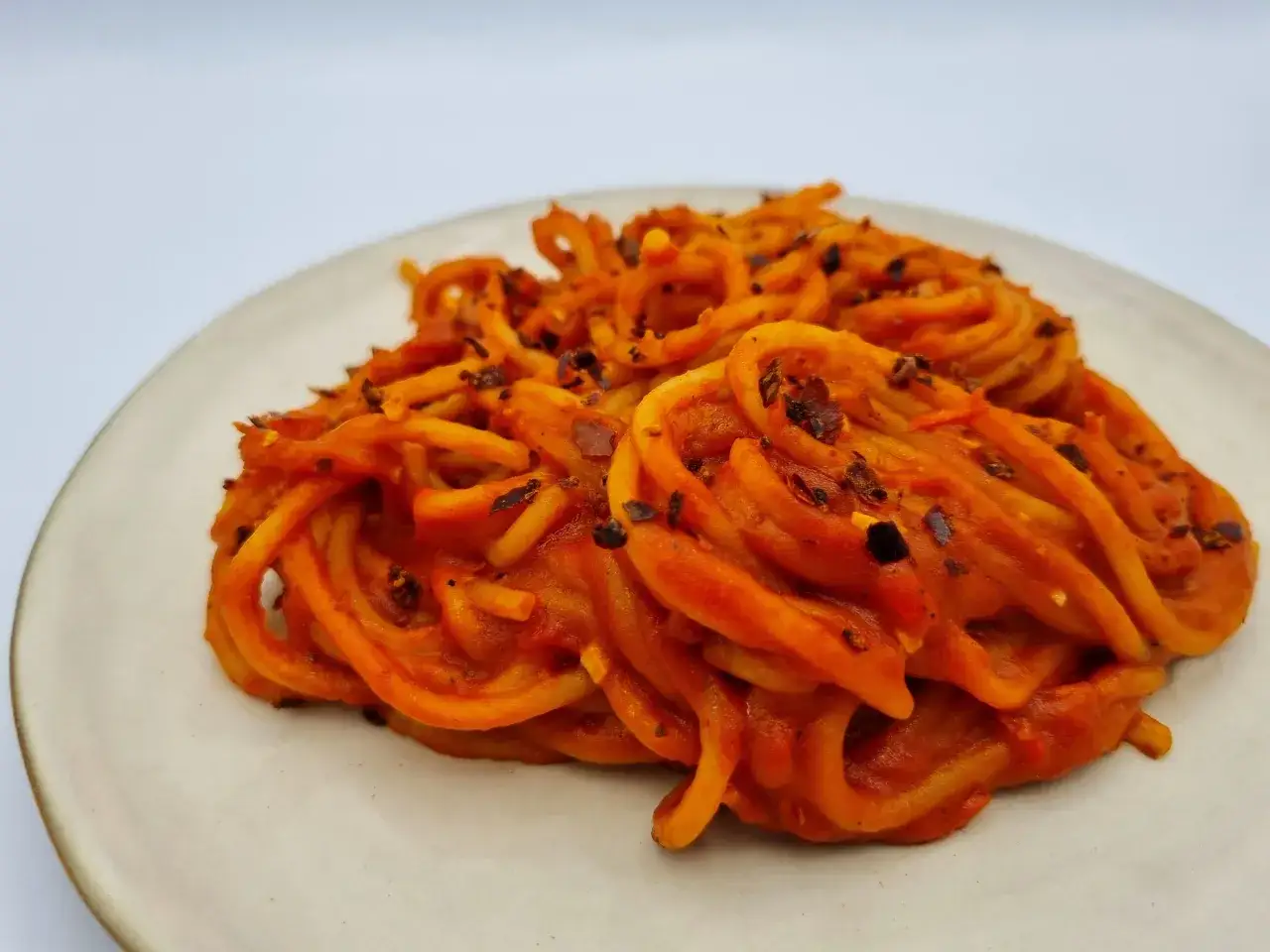 Spaghetti all'assassina, pikantne, pomidorowe danie z makaronem, posypane płatkami chili, na jasnym talerzu.