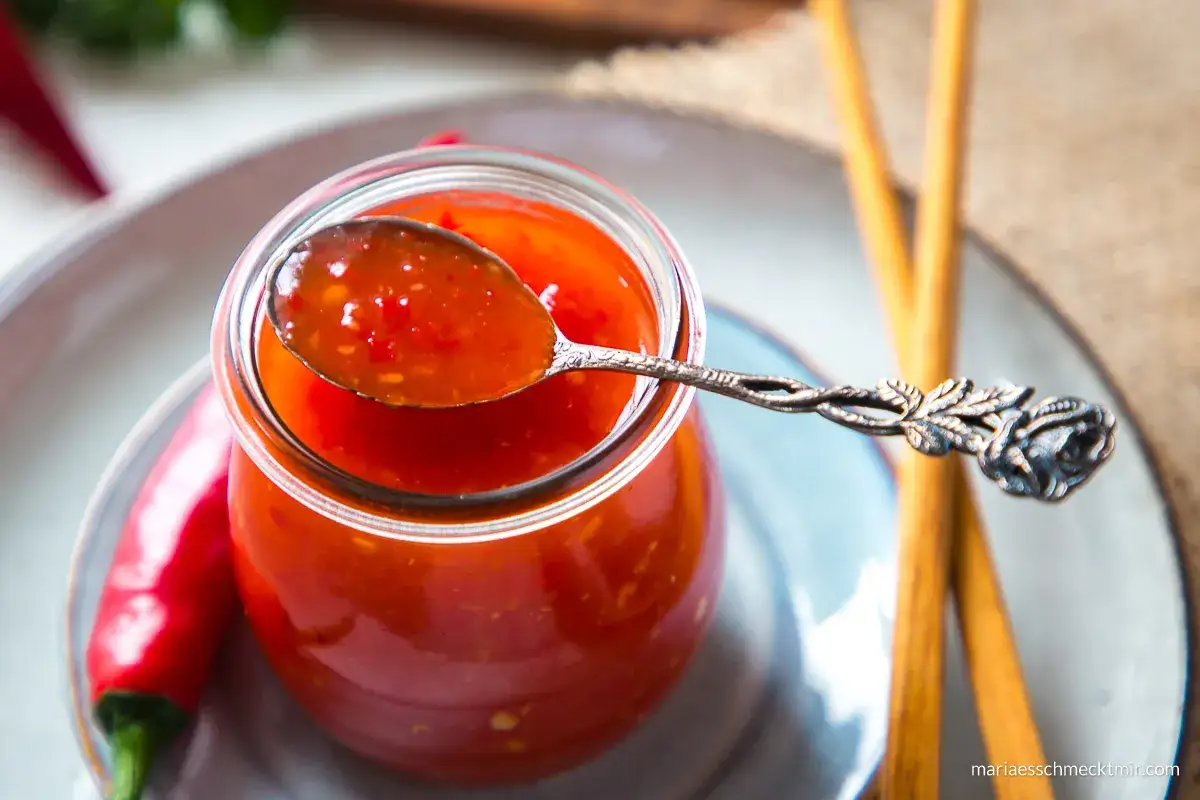 Selbstgemachte Chili-Sauce in einem Glas, mit einer Löffelprobe und frischen Chilis. Perfekt für alle, die Chili-Sauce selber machen wollen.