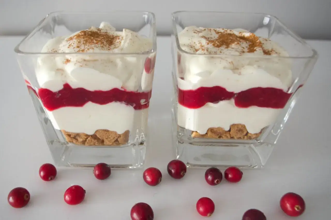 Dwa pucharki z deserem: warstwa ciastek, krem z mascarpone i białej czekolady, czerwony sos, posypane cynamonem.