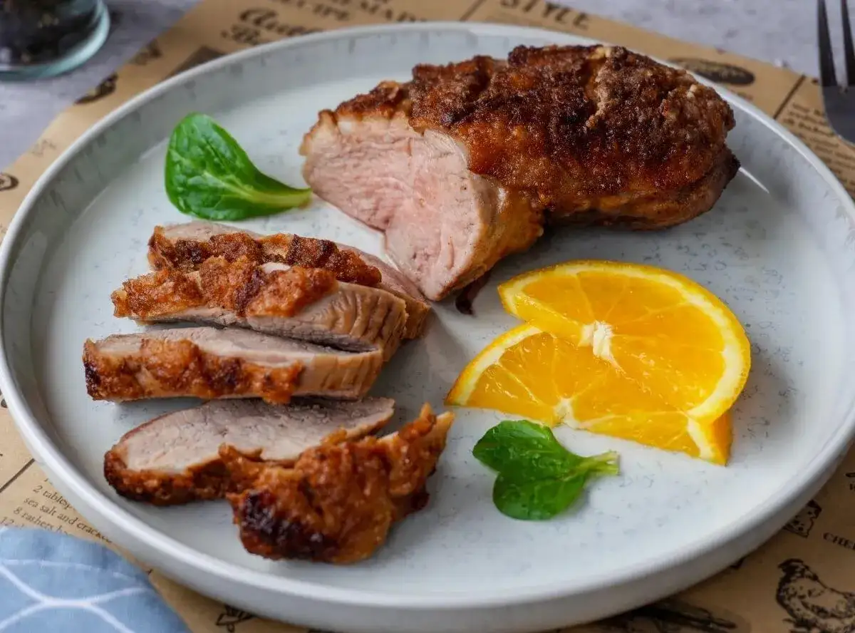 Saftige entenbrust im airfryer, perfekt gebräunt und in Scheiben geschnitten, serviert mit frischen Orangenspalten und grünen Blättern.