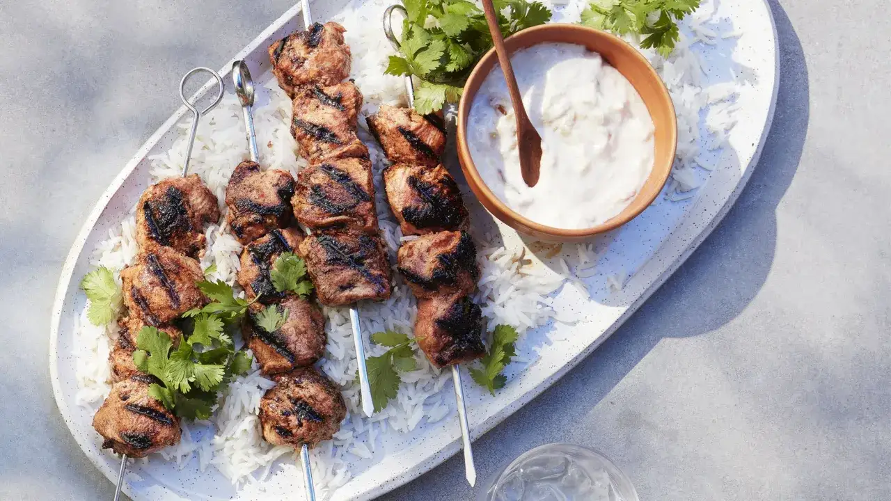 Grillade spett med shish tawook, serverade på en bädd av ris med en skål yoghurt och färsk koriander.