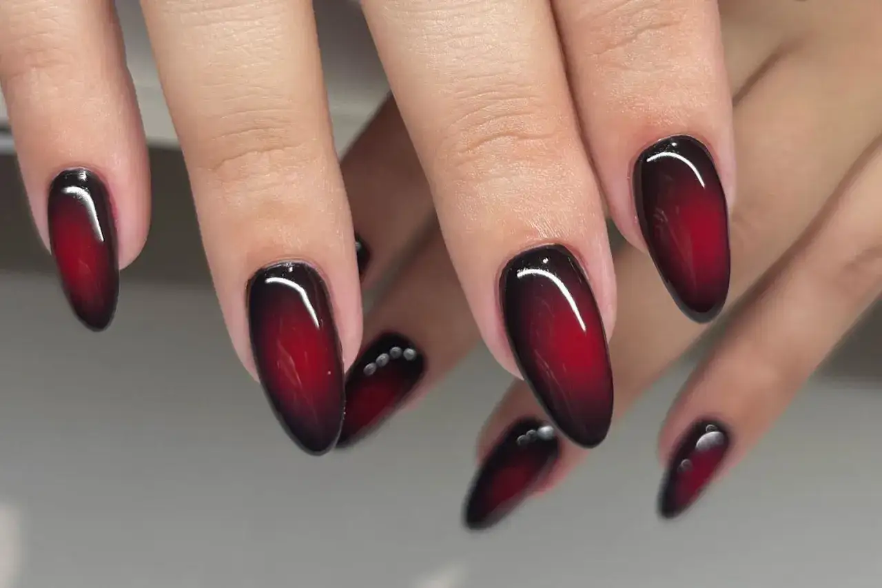 Dłonie z paznokciami w stylu aura nails, z efektem ombre od czerni do głębokiej czerwieni.