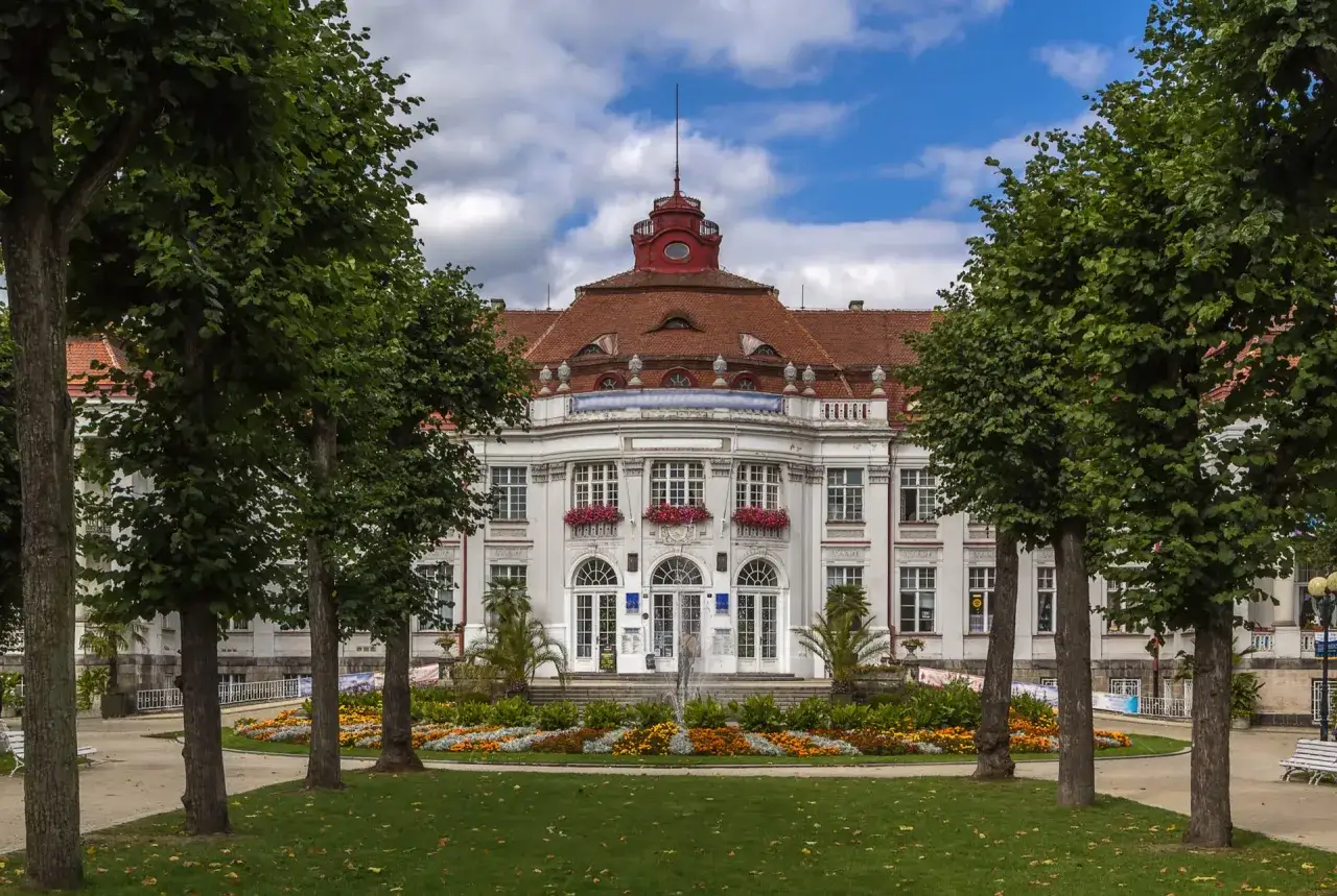 Piękny budynek w Karlowych Warach, z fontanną i kwitnącymi rabatami kwiatowymi przed wejściem. Idealne miejsce na relaks w termach.