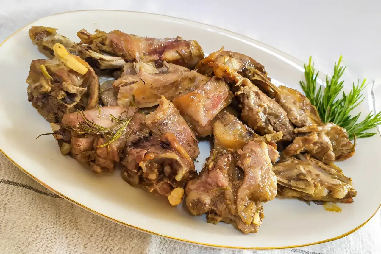 Succulento agnello al forno, cotto a puntino con aglio e rosmarino, servito su un piatto bianco bordato d'oro.